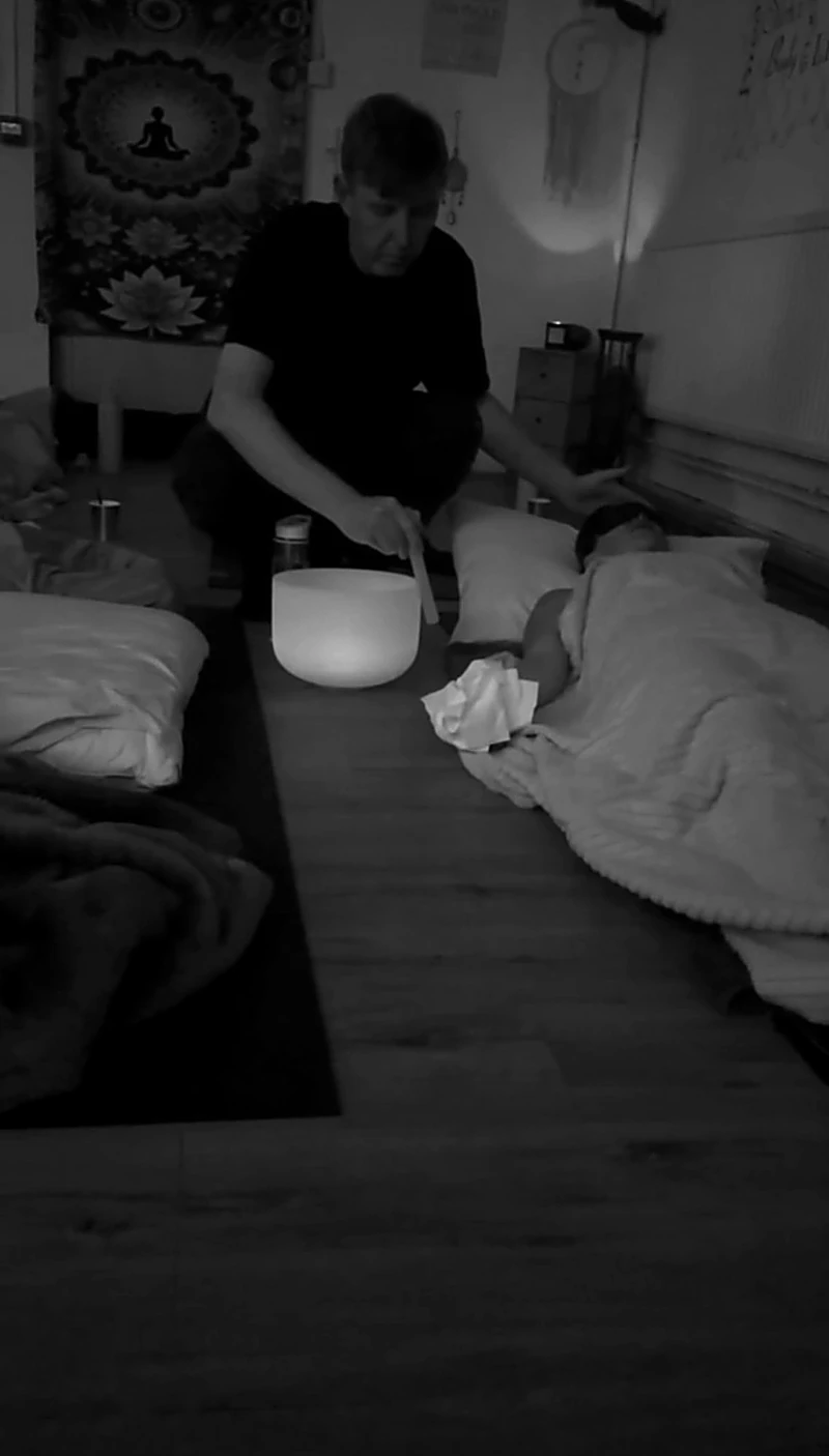 Nada Kari playing a crystal singing bowl beside a participant resting under a blanket