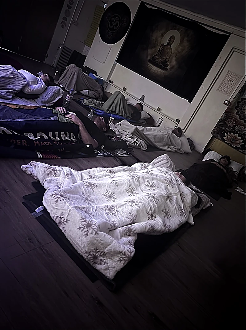 Participants resting on mats under blankets, wearing eye masks, during a Nada Kari group sound bath
